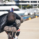 Homeless,Man,Riding,His,Bicycle,While,Carrying,Bags,And,Backpacks.