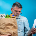 Surprised,Mature,Man,Looking,At,Store,Receipt,After,Shopping,,Holding